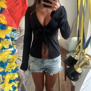 Svart omlottopp med knyt från Gina Tricot - Svart långärmad omlottopp från Gina Tricot i mjuk bomullsmix. Djup v-ringning och snygg knytning framtill som ger en trendig look. Perfekt till jeans eller kjol för en cool och enkel stil.