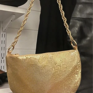 Guldig axelväska från Public Desire - Säljer en glittrig guldig axelväska från Public Desire med kedjehandtag. Väskan har ett mesh-liknande material som ger en riktigt festlig vibe och insida i satin. Perfekt för att lyfta vilken outfit som helst.Helt ny Mått 24x15 cm