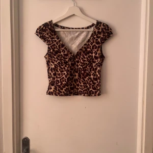 Leopardmönstrad croppad topp - Snygg croppad topp med leopardmönster i bruna och beige toner. Toppen har v-ringning framtill och korta ärmar, perfekt för dig som vill sticka ut. Figurnära passform och stretchigt material som sitter skönt på kroppen.