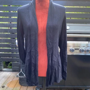 Svart kofta från Cubus XS - Svart kofta med långa ärmar och öppen front. Den har ett band i ryggen som kan knytas för att justera passformen. Perfekt för lager-på-lager-stilen. L: 72 cm 55% viskos 25% bomull 20% polyamid  Inga bilder när den sitter på mig! Katter finns i hemmet!