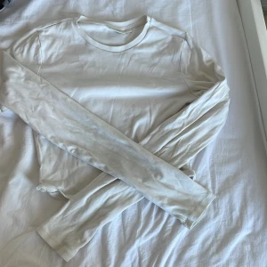 Vit långärmad basic tröja - Enkel och stilren vit långärmad tröja i mjuk bomull. Perfekt att ha som basplagg och funkar till allt. Tröjan har rund halsringning och en rak passform som gör den lätt att matcha med olika outfits. 