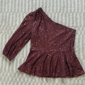 Rosa paljettopp oneshoulder - Säljer en glittrig festtopp från JDY med paljetter över hela ytan. Toppen har en snygg oneshoulder-design med lång ärm och volang nertill. Perfekt för dig som vill sticka ut med en festlig look. Stängs med dragkedja i sidan. Den är mer rosa i verkligheten än vad som tas upp på kameran