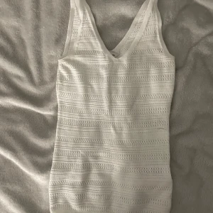 Vit ribbad linnetopp  XS - Säljer en vit linnetopp från C i storlek XS. Toppen har ett ribbat mönster med små hål och horisontella ränder, samt v-ringad hals. Perfekt för dig som gillar en enkel men ändå detaljerad look.