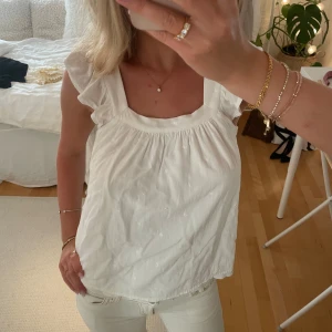 Vit blus med volangärmar - Supersöt vit blus med fyrkantig ringning och volangärmar. Lätt och luftig bomull med diskret broderat mönster. Perfekt för en fräsch och somrig look, passar till både jeans och kjol.