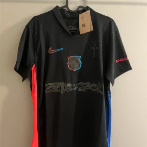 Svart FC Barcelona x Nike fotbollströja - Snygg svart FC Barcelona fotbollströja från Nike med coola detaljer i rött och blått på sidorna. Tryck med klubbmärke, Nike-logga och grafiska element framtill. Korta ärmar och sportig passform, perfekt för dig som vill sticka ut på planen eller läktaren.