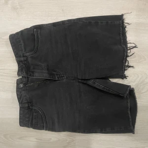 Svarta shorts med rå kant - Coola svarta shorts med rå, fransig kant nertill och klassiska jeansdetaljer som fickor och dragkedja. Perfekt för dig som gillar en avslappnad och edgy stil.