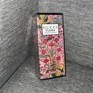Gucci Flora Gorgeous Gardenia EdP 100ml - Gucci Flora Gorgeous Gardenia Eau de Parfum i 100 ml flaska. Förpackningen är rosa med färgglada blommor och gröna blad, vilket ger en lyxig och feminin känsla. Parfymen är en blommig doft och kommer i en rektangulär kartong med tydlig Gucci-logga.