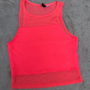 Neonrosa mesh-linnetopp från H&M Divided - Neonrosa linnetopp från H&M Divided med meshdetaljer upptill och nedtill. Toppen är ärmlös och har en croppad passform som ger en sportig vibe. Perfekt för att sticka ut med en färgstark look. Materialet är syntet och känns lätt och luftigt. Finns skavanker se bilderna