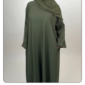 Olivgrön abaya med stängda ärmar - Snygg olivgrön abaya med lös passform och stängda ärmar. Klänningen har en enkel och stilren design utan mönster, perfekt för dig som gillar minimalistiskt mode. Tillverkad i ett mjukt och lätt material som faller fint. Från luude collection