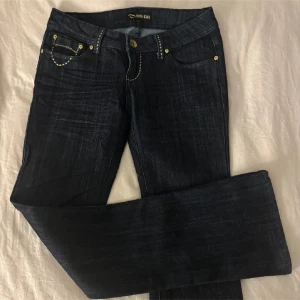 Mörkblå vintage jeans - Snygga lågmidjade mörkblå jeans från Miss Kiss med kontrasterande gul söm och detaljerade bakfickor med dragkedja. Raka/ utsvängda ben