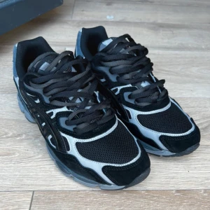 Svarta och grå Asics sneakers - Säljer mina svarta ASICS GEL-NYC i modellen “Triple Black” med snygg dubbelsnörning. 