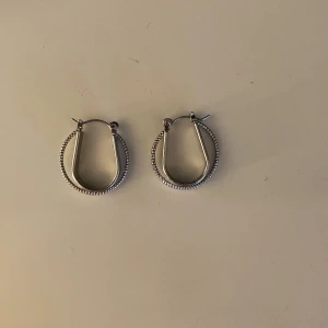 Silvriga hoops örhängen - Snygga silvriga hoops med en unik, lite kantig form och detaljerad kant. Perfekta för att ge din look lite extra edge. Passar dig som gillar stilrena smycken med en twist.
