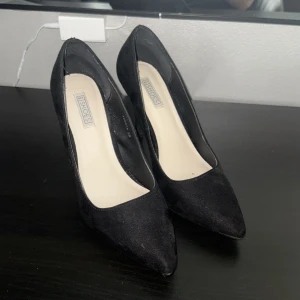 Svarta pumps  - Klassiska svarta pumps i storlek 39 från NLY Shoes med spetsig tå och hög klack. Skorna är i mockaliknande material och har en elegant, tidlös design som passar till många olika outfits. Perfekta för dig som gillar stilrena och snygga skor.