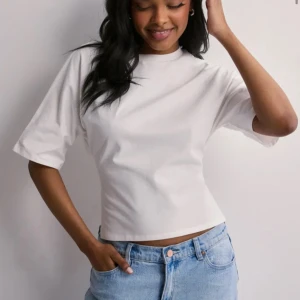 Vit croppad topp med knyt i ryggen - Snygg vit croppad topp med korta ärmar och cool öppen rygg som knyts med breda band. T-shirten har en enkel och clean look framtill men överraskar med knyt och öppen detalj bak. Perfekt till jeans eller kjol för en trendig vibe.