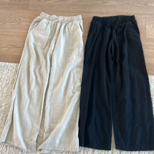 2 par vida linnebyxor från Lindex - Två par sköna och luftiga linnebyxor från Lindex, ett par i beige och ett par i svart. Båda har resår i midjan och vida ben för en chill och avslappnad look. Perfekta för varma dagar eller när du vill ha det bekvämt.