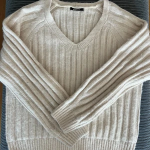 Beige ribbstickad tröja Gina Tricot - Supermysig beige ribbstickad tröja från Gina Tricot med v-ringning och långa ärmar. Tröjan har en relaxed passform och är perfekt för lager-på-lager. Materialet är mjukt och ger en chill vibe till din outfit.