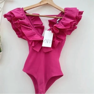Rosa volangbody från ZARA - DEN POPULÄRA! Superfina volang bodyn i stark rosa färg från ZARA med stora volanger längs axlarna och djup v-ringning. ALDRIG ANVÄND!