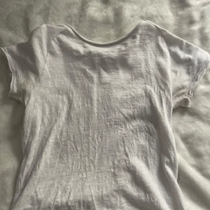 Vit basic t-shirt i bomull - Enkel vit t-shirt med korta ärmar och rund hals. T-shirten är tillverkad i mjuk bomull och har synliga sömmar längs ryggen och axlarna för en avslappnad look. Perfekt att matcha med jeans eller shorts för en clean stil.