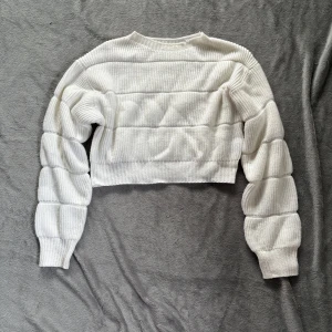 Vit croppad stickad tröja från SHEIN - Superfin vit croppad stickad tröja från SHEIN med ribbad struktur och unika puffade ärmar. Tröjan har rund halsringning och är perfekt för dig som gillar trendiga detaljer och en chill vibe. Passar snyggt till både jeans och kjol.
