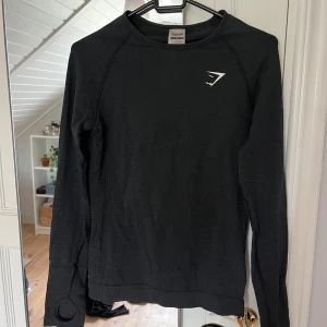 Svart långärmad träningströja Gymshark - Svart långärmad träningströja från Gymshark med tumhål i ärmsluten. Tight passform och ventilerande material som passar perfekt till gymmet eller löprundan. Använd men i fint skick