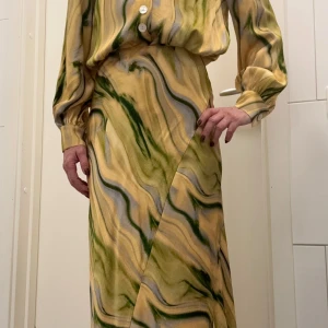Långkjol från & Other Stories i grönt mönster - Säljer en långkjol samt blus, paketpris från & Other Stories med unikt abstrakt mönster i grönt, gult och beige. Kjolen är tillverkad i ett mjukt, lätt material som faller snyggt. Perfekt för dig som vill sticka ut med coola färger och vågigt mönster. Använd vid ett tillfälle.