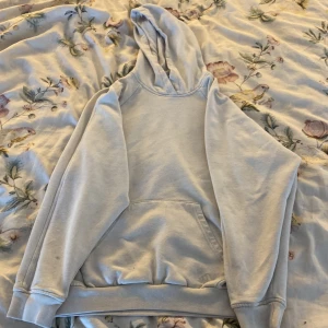 Ljusgrå hoodie från Adidas - Enkel och stilren ljusgrå hoodie från Adidas med broderad logga på fickan. Klassisk känguruficka, huva och långa ärmar. Perfekt för chill dagar eller när du vill ha en clean look. Mjuk och skön i bomullsmix. Liten fläck på högra armen.
