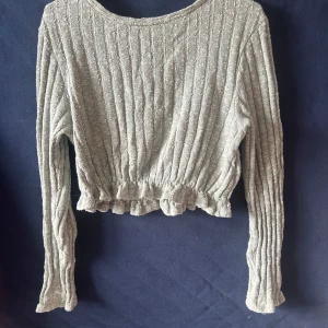 Ljusgrå ribbad croppad tröja NA-KD - Superfin ljusgrön croppad tröja från NA-KD med ribbad struktur och volangkant nedtill. Tröjan har långa ärmar och en mjuk, stickad känsla som gör den både snygg och bekväm. 