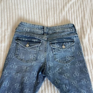 Blå lowaisted bootcut jeans från HM - Snygga blå bootcut jeans från H&M med all-over logomönster i ljusblått. Byxorna är lågmidjade och jättefina bakfickor. Byxorna är en collab med black pink. Jag är 1,73 för referens passa på att köpa dessa fina byxor!