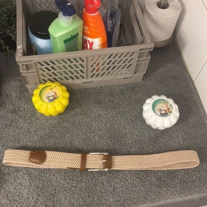 Beige flätat bälte med skinn-detaljer - Snyggt beige flätat bälte med bruna skinn-detaljer och silvrigt spänne. Bältet har ett stilrent mönster och passar perfekt till jeans eller chinos. Ger en clean och fräsch look till outfiten.