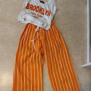 orange linnebyxor med linne . Bra använd men bra ändå. - Säljer ett par snygga orange linnebyxor med vita vertikala ränder och breda ben. Byxorna har hög midja, resår och snörning i midjan samt stora fickor framtill. Perfekta för en chill och färgglad look i sommar.