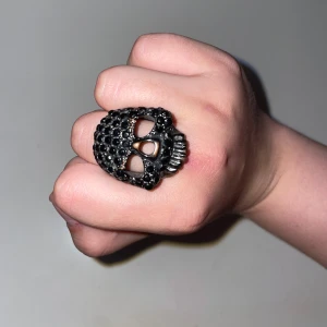 Svart dödskallering med stenar - Cool ring i form av en dödskalle, täckt med svarta glittrande stenar. Ringen är i metall och har en tydlig, edgy vibe som sticker ut. 