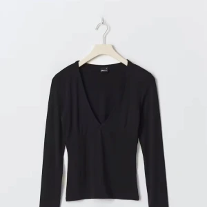 Svart v-ringad topp Gina Tricot XS - Svart långärmad topp från Gina Tricot i storlek XS. Modellen är figurnära med djup v-ringning och croppad passform. Lite sliten mellan brösten annars som helt ny