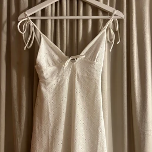 Söt klänning  - Söt vit klänning med knytband vid axlarna och ett diskret blommönster. Klänningen har en v-ringad design och är perfekt för sommarens varma dagar. Den är ärmlös och har en lätt och luftig känsla. Skiv gärna för fler bilder. 