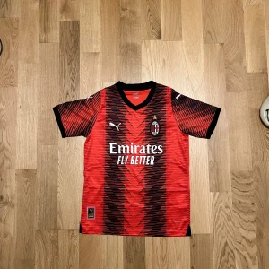 AC Milan T-shirt - Säljer en snygg AC Milan fotbollströja i rött och svart från Puma. Tröjan har korta ärmar och ett coolt mönster med klubbens emblem på bröstet. Perfekt för alla Milan-fans! 🖤❤️säljer den eftersom den inte passade när jag fick den i födelsedagspresent