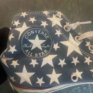 Converse All Star - Snygga Converse All Star skor med vita stjärnor. Klassisk hög modell med snörning och vit sula med röd rand. 
