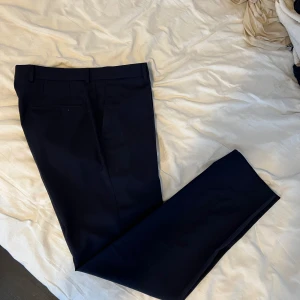 Oscar Jacobson kostymbyxor - Marinblå kostymbyxor från Oscar Jacobsson. Slim fit. Stl 50. Mycket bra skick, använda fåtal gånger.