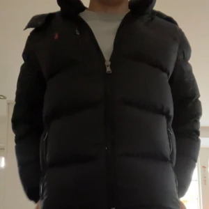 Svart dunjacka från Ralph Lauren - Säljer en stilren svart dunjacka från Ralph Lauren. Perfekt för kyligare dagar med sin pufferdesign som håller värmen. En klassisk och tidlös modell för garderoben.