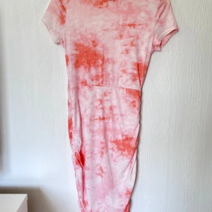 Rosa och orange klänning - Trendig rosa och orange klänning med batikmönster. Den har korta ärmar och en snygg snörning på sidorna som ger en cool detalj. Perfekt för sommarens alla tillfällen!