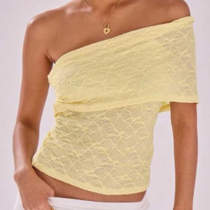 Gul offshoulder topp - Snygg gul offshoulder topp i spetsmaterial. Perfekt för sommarens varma dagar. Den har en unik design med en axel bar och en elegant spetsstruktur som ger en romantisk känsla.