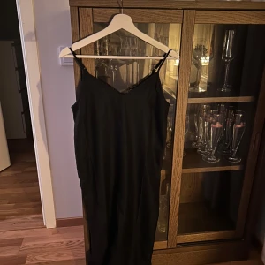 Svart klänning - Elegant svart  klänning med smala axelband och v-ringad design. Perfekt för en stilren look. Lite stor i storleken