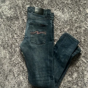 Mörkblå jeans från Nudie Jeans - Galet snygga mörkblå jeans från Nudie Jeans med tillverkade i slitstarkt denim. En reparation har skett vid skrevet annars är skicket perfekt. Nypris 1800. Hör av dig vid frågor!