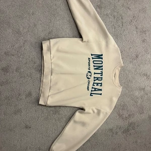 Beige tröja från Gina Tricot - Säljer en beige tröja från Gina Tricot med texten 'Montreal Sports Camp' i blått på framsidan. Tröjan har långa ärmar och en rund halsringning. Perfekt för en avslappnad stil. Storlek S och är knappast använd. Kontakta mig för fler bilder!