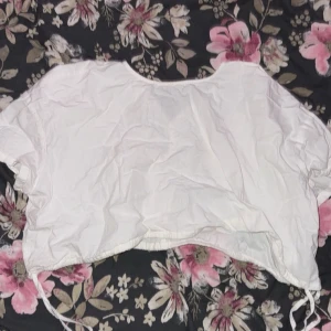 Vit kortärmad blus med knytband - Säljer en vit blus med korta ärmar och knytband i nederkant. Perfekt för en avslappnad stil. Blusen har en lös passform och är tillverkad i ett lätt material.