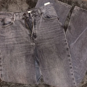 Grå/svarta jeans - Snygga grå jeans med en 70s high flare fit från Levi's. De har en traditionell femficksdesign och en knappgylf. Perfekta för en avslappnad stil.