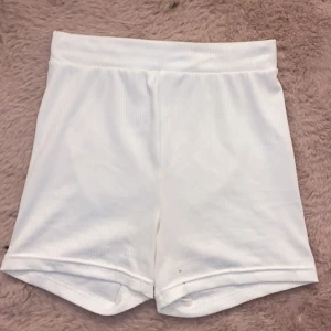 Vita ribbade cykelshorts - Säljer ett par vita ribbade cykelshorts med hög midja. Perfekta för en avslappnad stil. De är tillverkade i ett mjukt och bekvämt material som passar bra för varma dagar. Men har 2 små svarta fläckar på som syns på svarta bilden men absolut inget man tänker på🥰