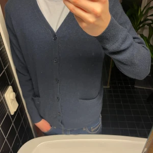 Mörkblå kashmirkofta  - Säljer en stilren mörkblå kofta i 100% kashmir. Koftan är en cardifan med knappar framtill och två praktiska fickor. Perfekt för lager-på-lager under kyligare dagar.