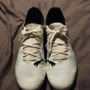 Fotbollsskor, Puma Future 7 play Fg/ag  - Snygga vita fotbollsskor från Puma med svarta detaljer och en färgglad sula i rosa och blått. Skorna har snörning och är designade för optimal prestanda på planen. Perfekta för den som vill sticka ut med stil.  Använda 2-3 gånger. 