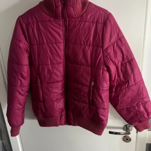 Rosa quiltad jacka - Säljer en snygg rosa quiltad jacka från Yessica. Jackan har en dragkedja framtill och ribbade muddar vid ärmslut och nederkant. Insidan är fodrad med mjukt material för extra värme. Perfekt för kyligare dagar!