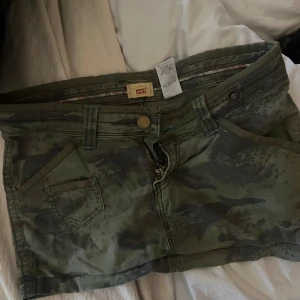 Camouflage kjol från Levi's - Säljer ett par coola camouflagefärgade kjol från Levi's. De har en knapp och dragkedja framtill samt praktiska fickor. Perfekta för sommar 