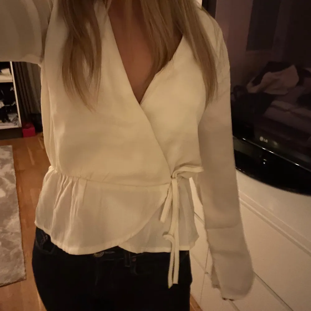 Säljer en stilren vit omlottblus med knytband i midjan. . Yläosat.
